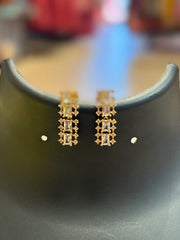 Elegant gold-toned earrings with rectangular and round clear stones displayed on black stand at Anandi Fashions