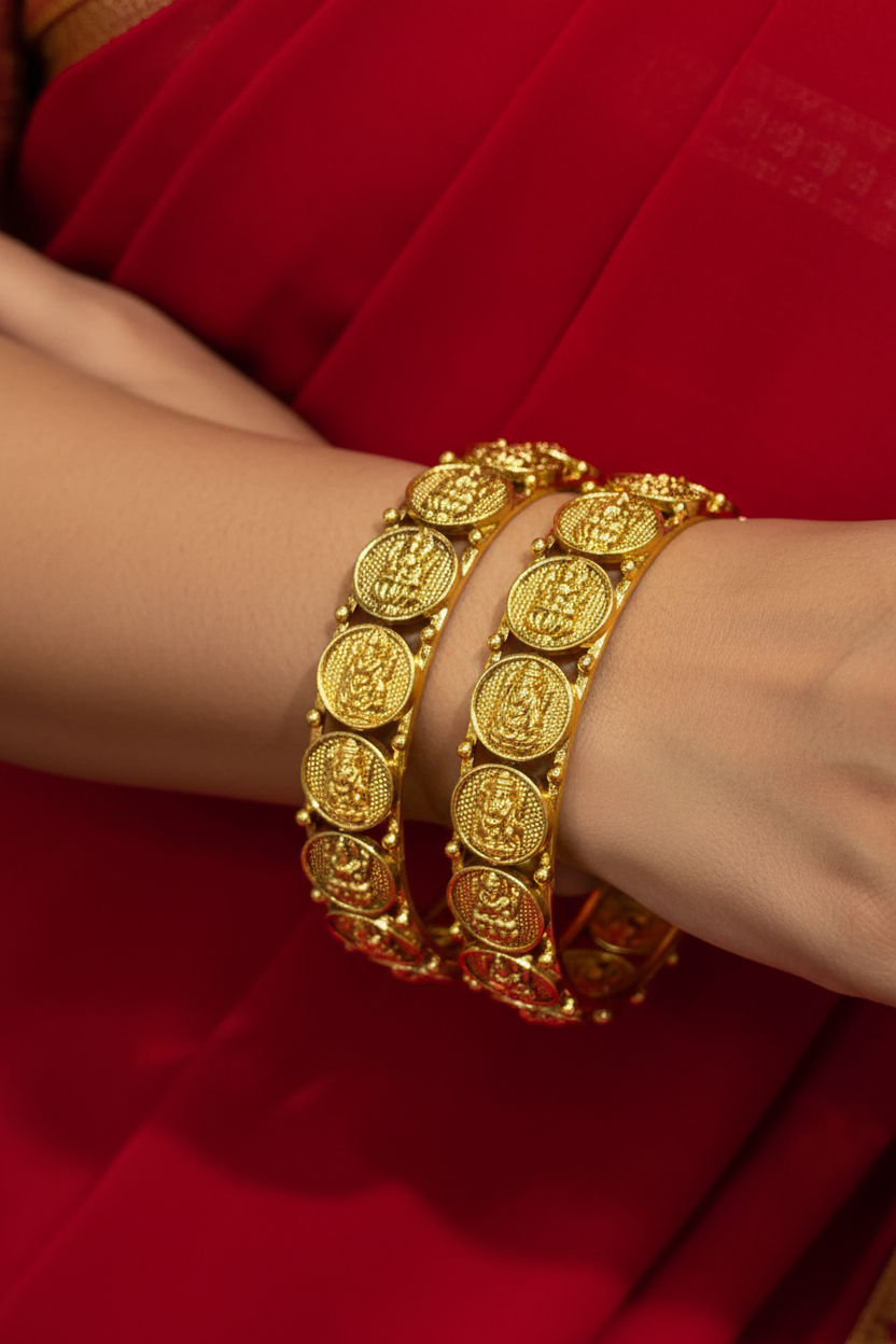 Close-up of a woman's hands wearing gold ethnic bangles with detailed temple coin designs, paired with a red saree