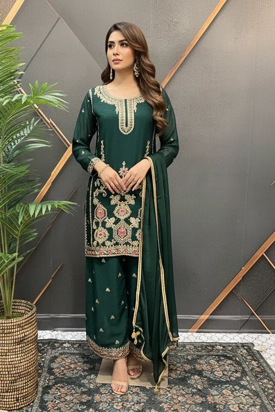 Woman in dark green embroidered Indian ethnic wear with dupatta, standing by decorative plant indoors