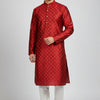 Man wearing red patterned silk kurta with white churidar and traditional sandals against grey background