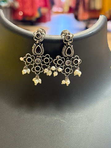 Silver-tone floral ethnic earrings with black stones and dangling white pearls on display