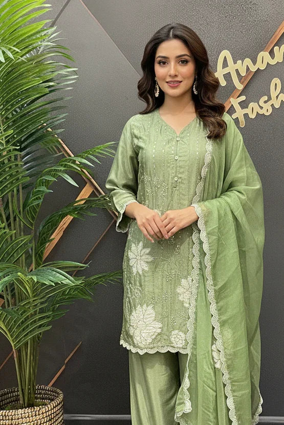Woman in a green outfit standing in front of a 'Anandi Fashions' branded wall.