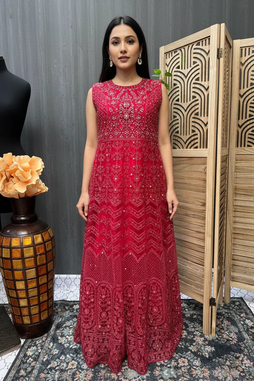 Woman wearing a red sleeveless embroidered ethnic gown standing indoors with decorative vase and wooden partition