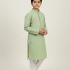 Boy in light green embroidered Indian kurta with white churidar and traditional shoes, studio background