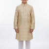 Young boy wearing beige embroidered Indian ethnic kurta with white churidar and traditional jutti shoes