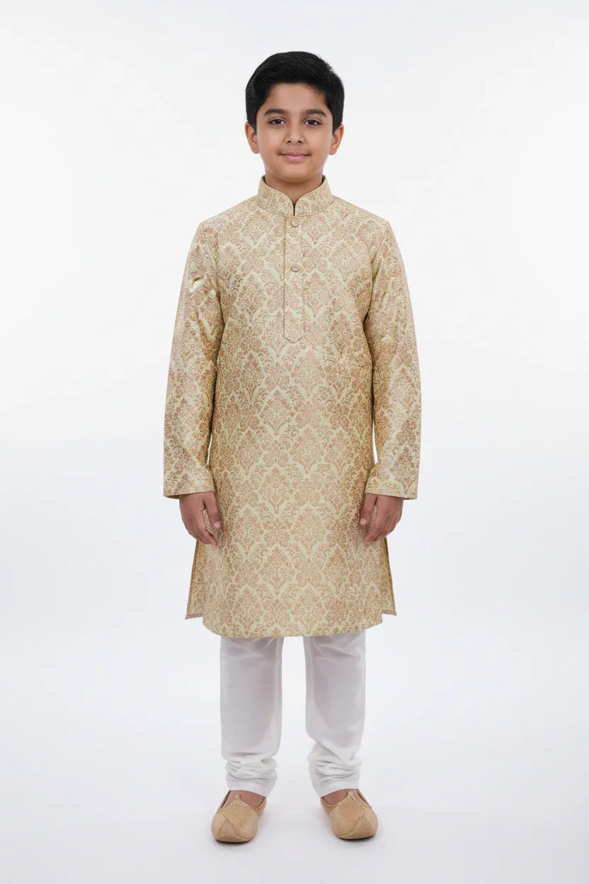 Young boy wearing beige embroidered Indian ethnic kurta with white churidar and traditional jutti shoes