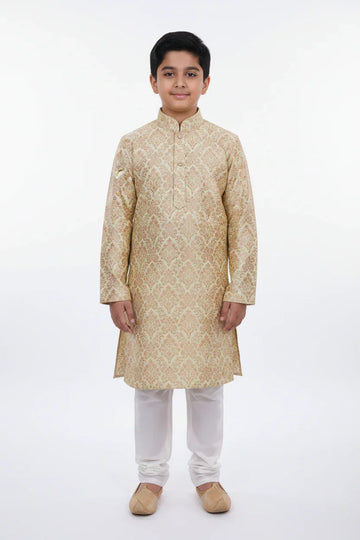 Young boy wearing beige embroidered Indian ethnic kurta with white churidar and traditional jutti shoes