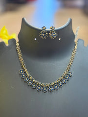 Gold-tone necklace and matching earrings set with blue floral designs displayed on black stand