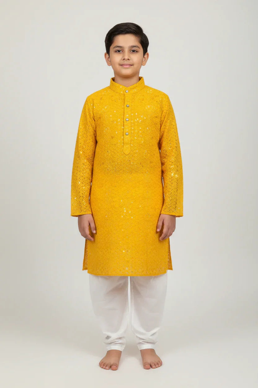 Boy wearing yellow embellished traditional Indian kurta with white churidar pants standing barefoot