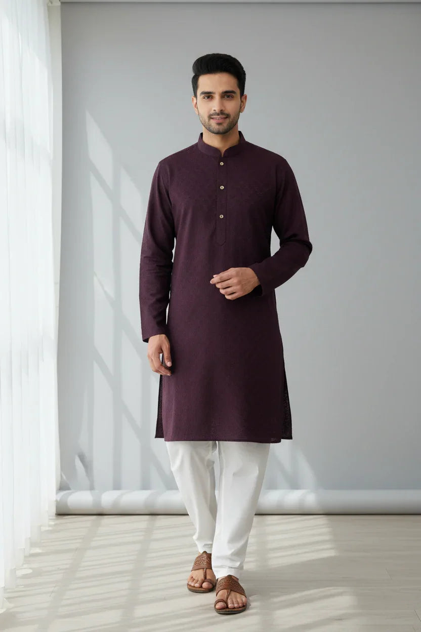 Man wearing dark purple ethnic kurta with white pajama and brown sandals in a bright room