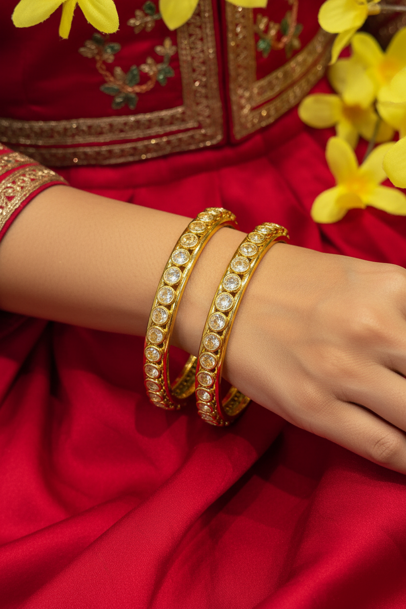 Close-up of hand wearing gold and diamond-studded bangles paired with red embroidered Indian ethnic wear and yellow flowers
