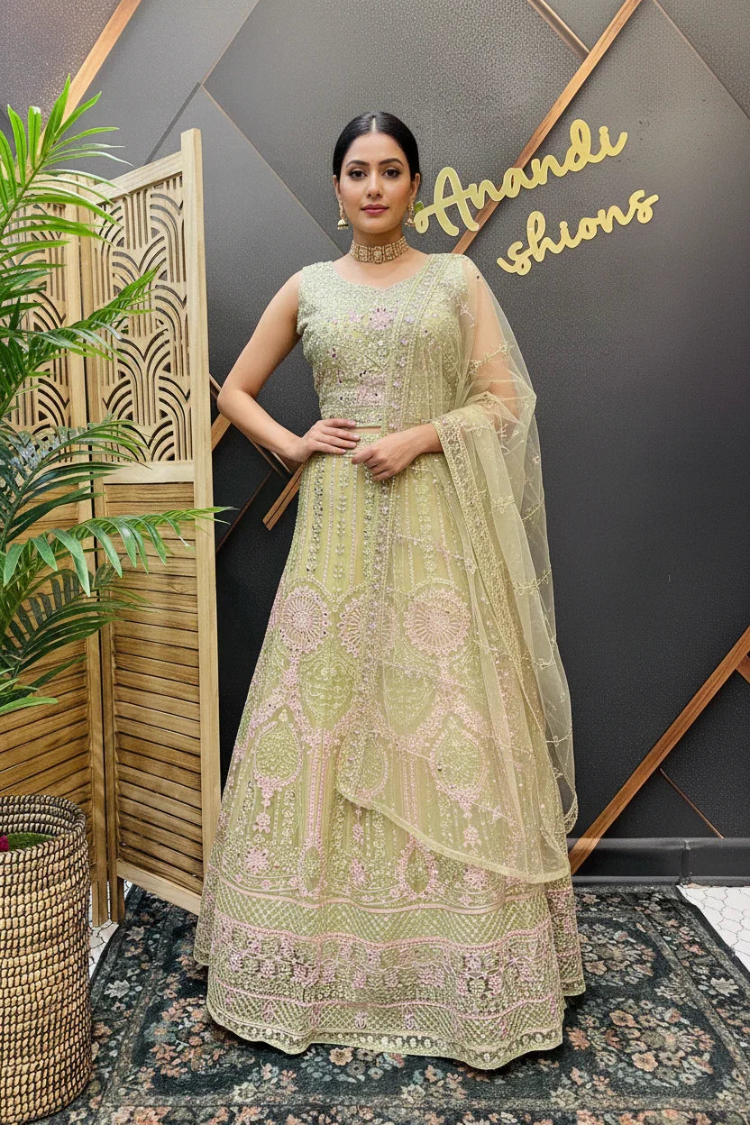 Woman wearing green embroidered Indian lehenga with matching dupatta, standing indoors by wooden screen and plant at Anandi Fashions