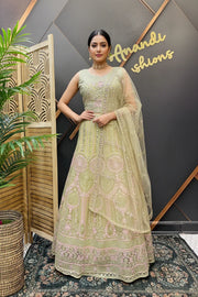 Woman wearing green embroidered Indian lehenga with matching dupatta, standing indoors by wooden screen and plant at Anandi Fashions