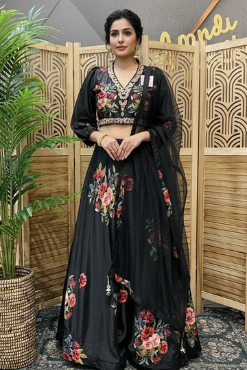 Woman in a black floral dress standing in front of a wooden screen with a plant to her left.