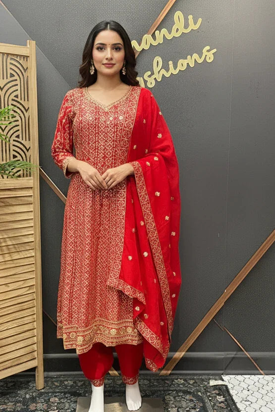 Woman in a red traditional outfit standing in front of a decorative wall with 'Kandhi' branding.