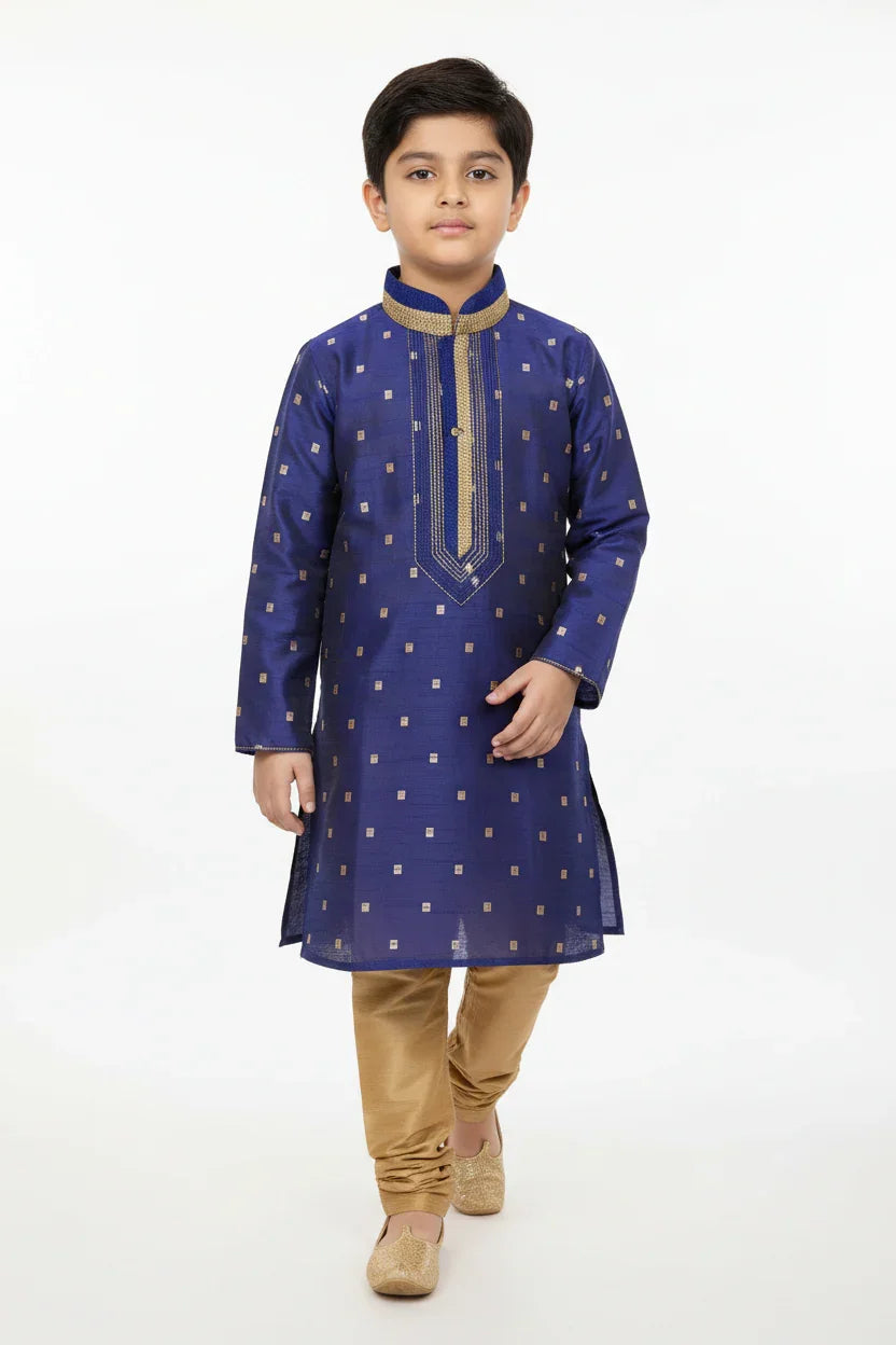Boy in blue embroidered kurta with gold churidar pants and traditional Indian footwear on white background