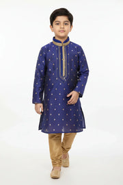 Boy in blue embroidered kurta with gold churidar pants and traditional Indian footwear on white background