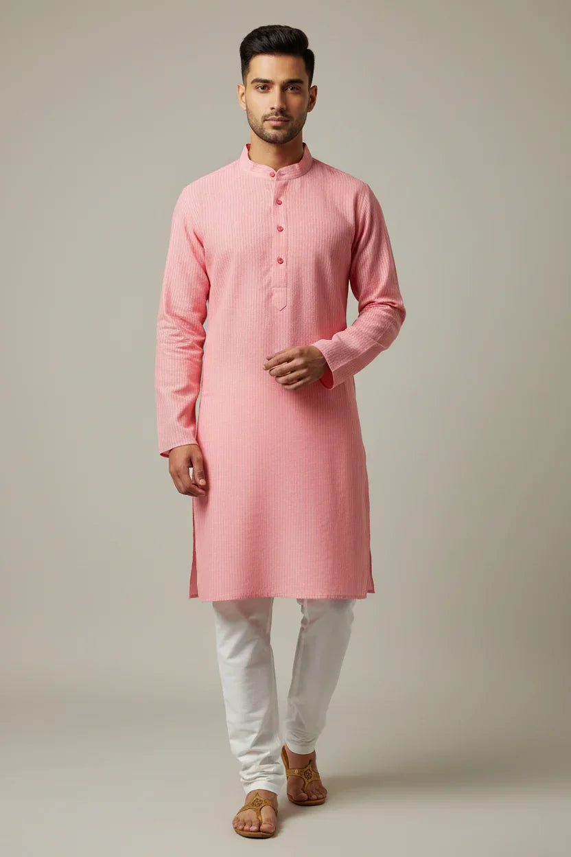 Man wearing pink Indian ethnic kurta and white churidar with traditional sandals on plain background