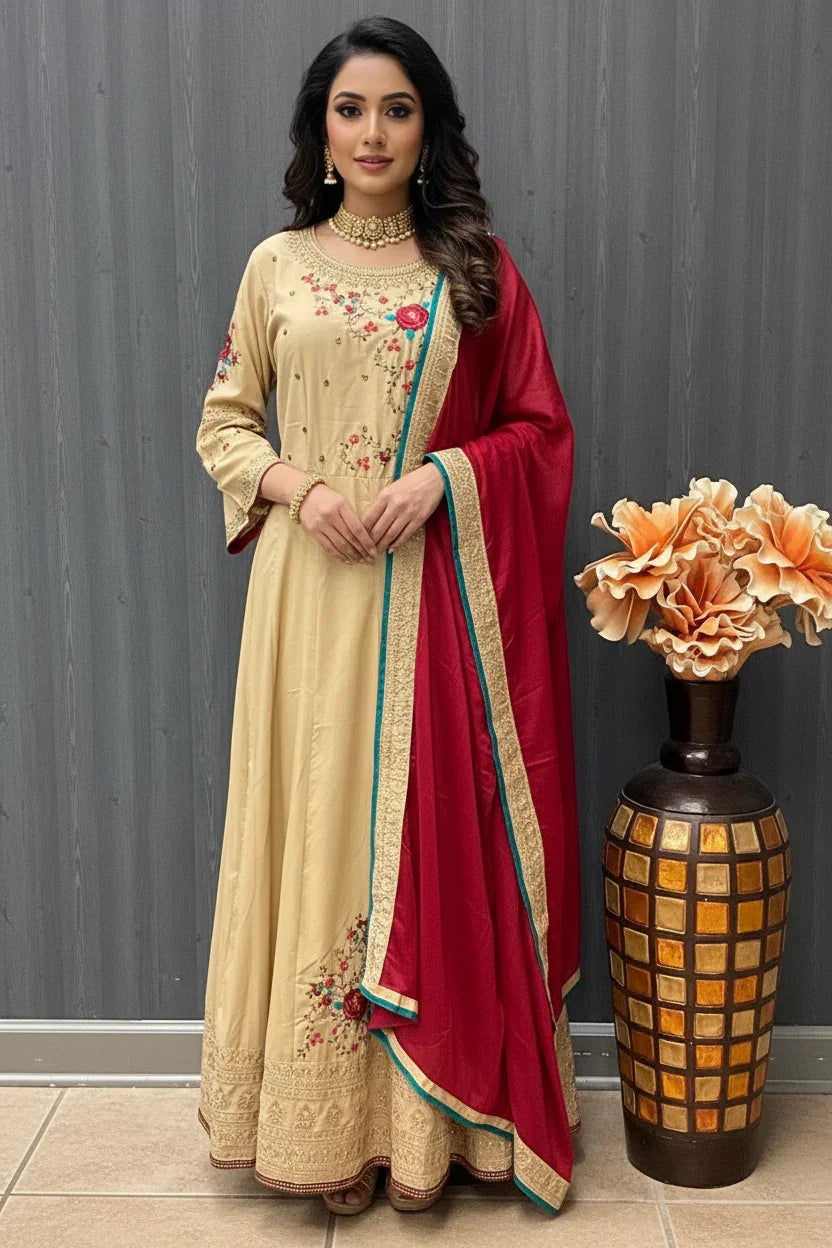 Woman in cream Indian ethnic dress with floral embroidery and red dupatta, standing by decorative vase with flowers