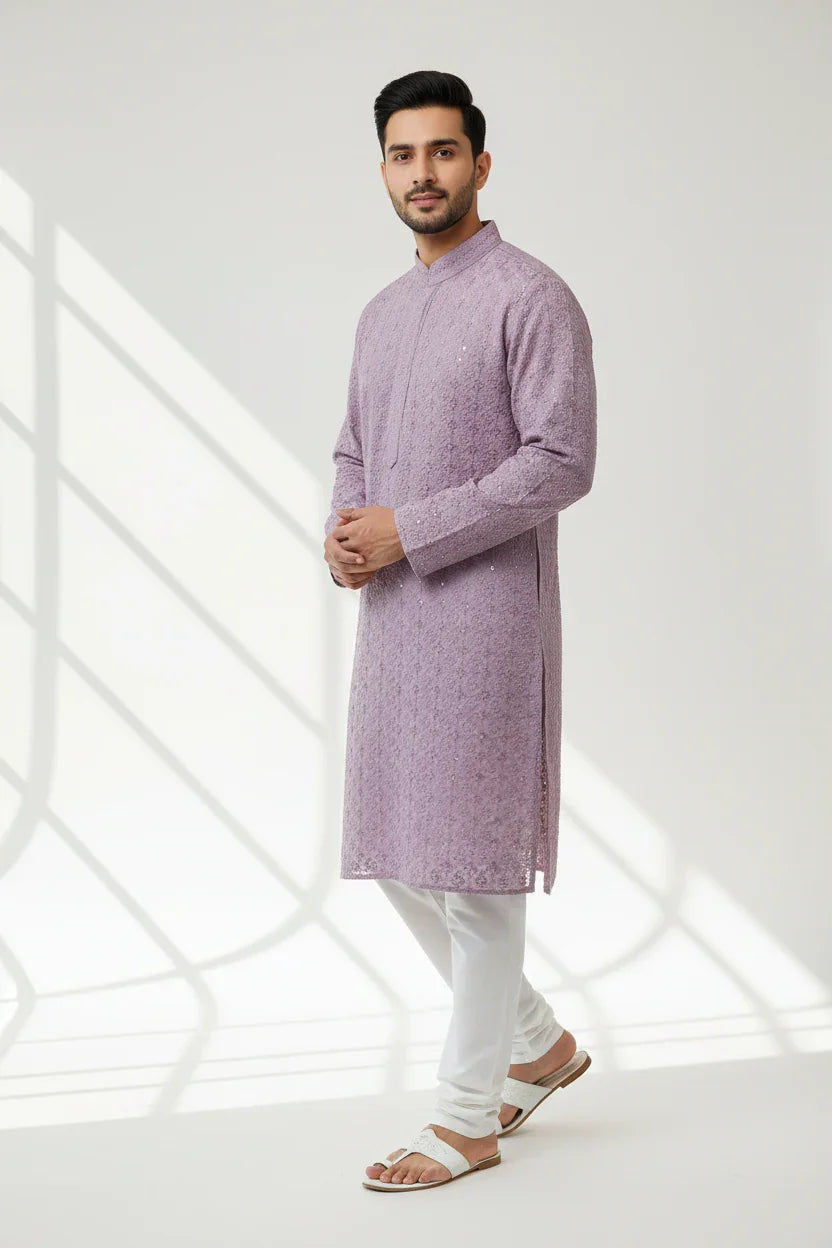 Man in lavender textured Indian kurta with white churidar pants and white sandals, standing in soft natural light