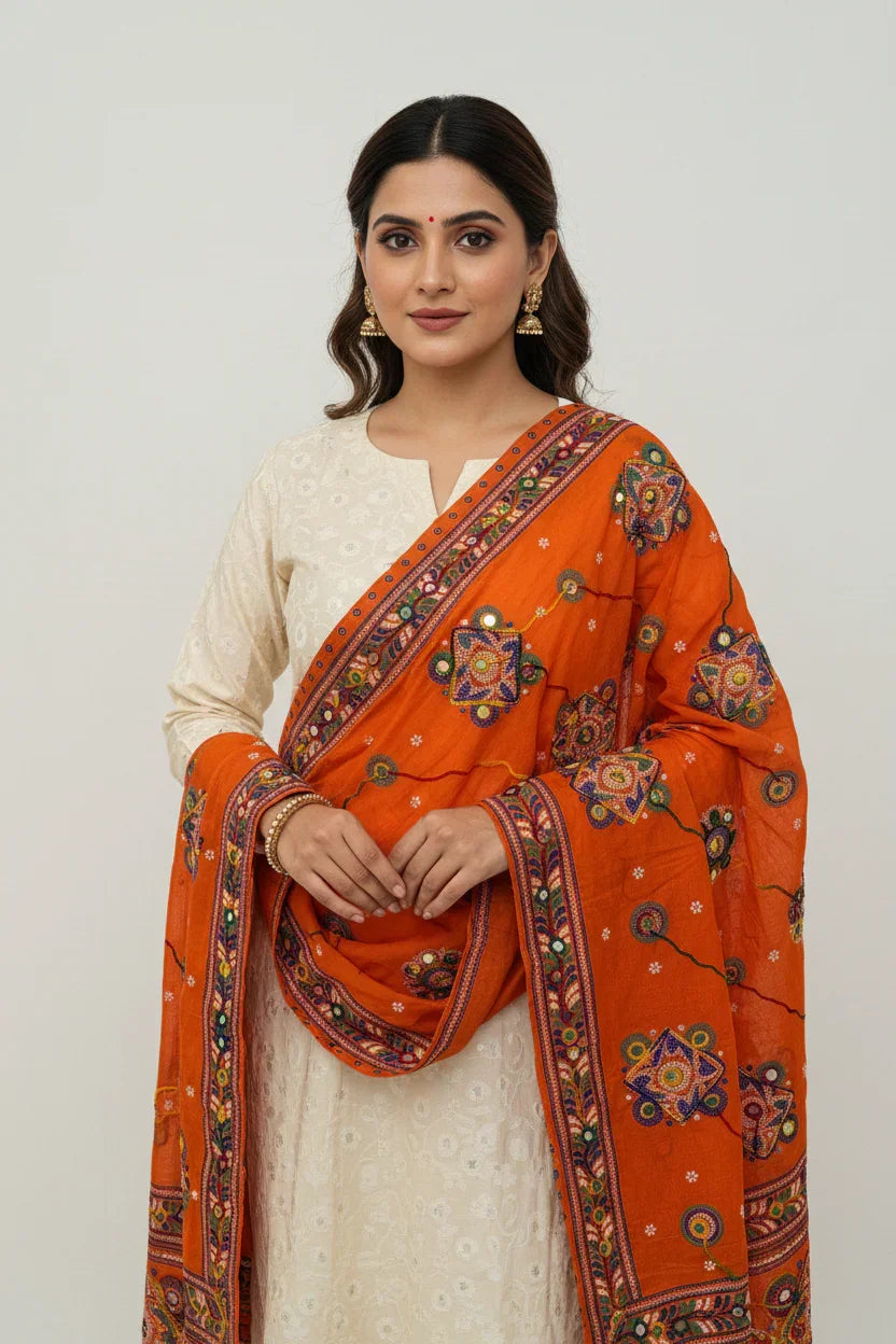 Woman wearing cream Indian ethnic wear with vibrant orange embroidered dupatta and traditional earrings