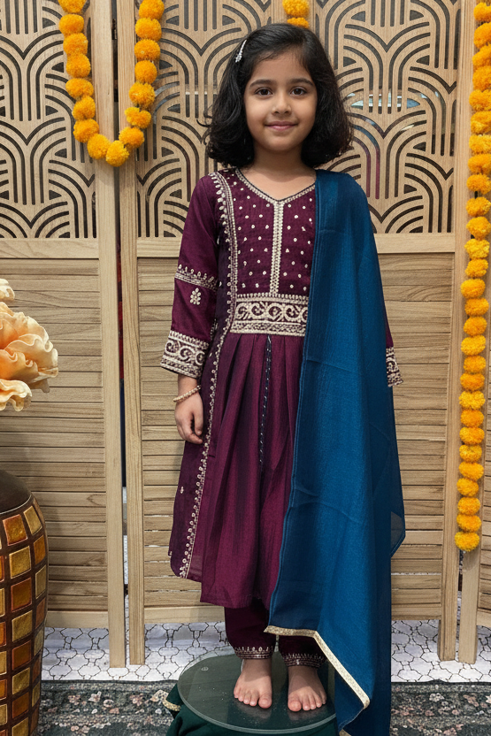 Young girl in traditional attire standing in a decorated room with floral arrangements.