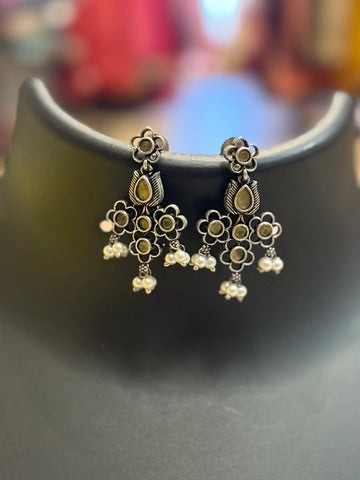 Silver floral design ethnic earrings with pearl danglers, displayed on black stand