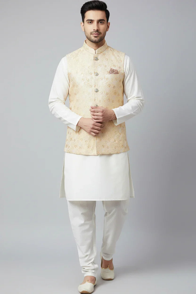 Man wearing cream embroidered Nehru jacket with white kurta pajama and mojari shoes against grey background