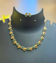 Gold necklace and matching earrings with green gemstones displayed on black stand at Anandi Fashions