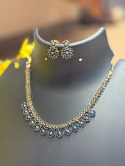 Gold necklace and earrings set with blue floral designs displayed on black stand at Anandi Fashions