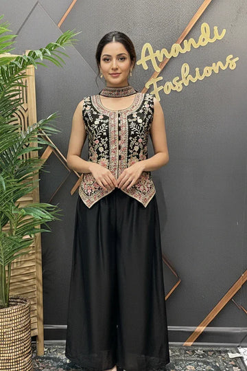 Woman in a stylish outfit standing in front of a branded wall with plants on either side.