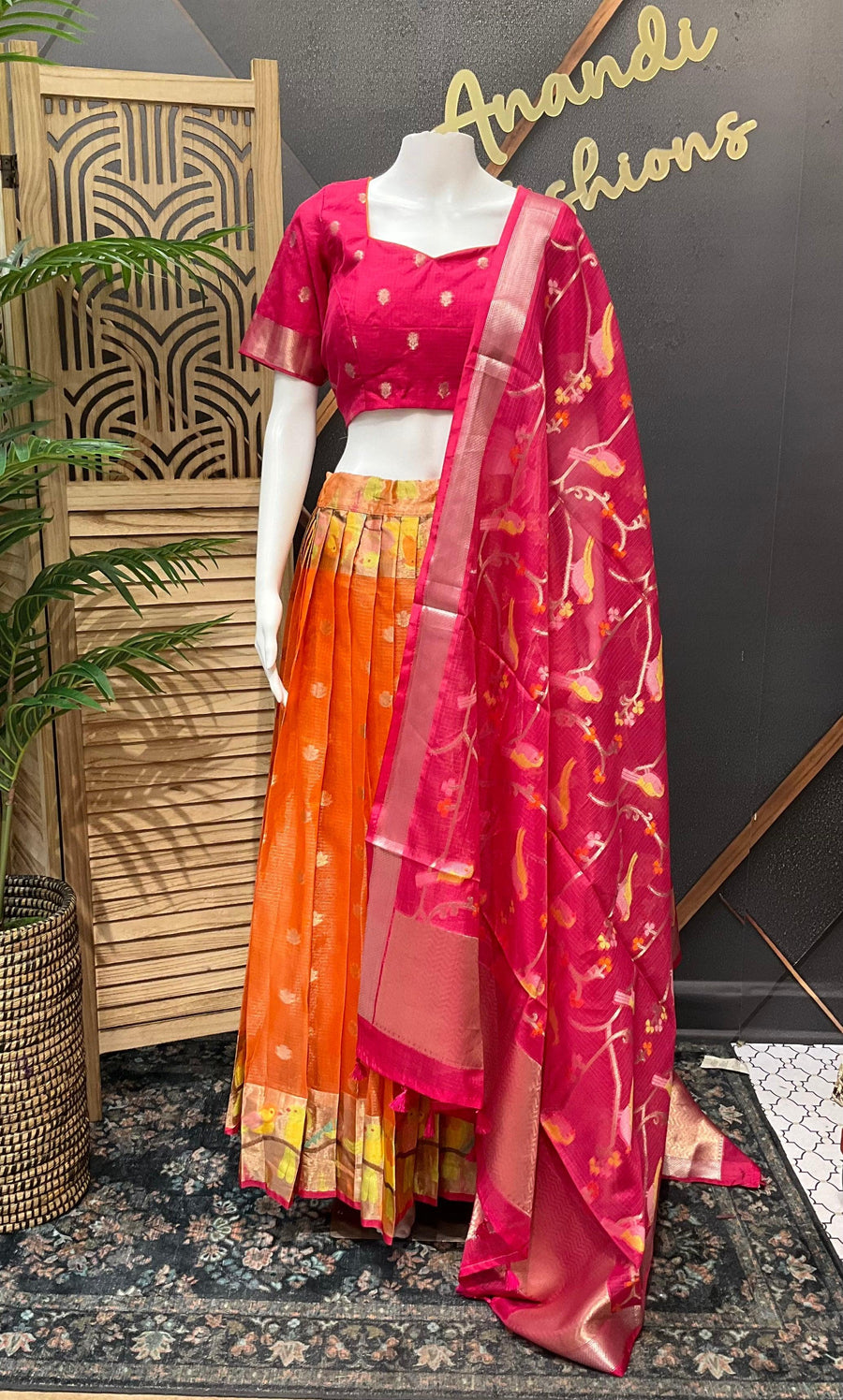 Mannequin in bright pink embroidered blouse, orange pleated lehenga, and floral printed pink dupatta at Anandi Fashions