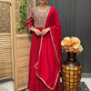 Woman in red embroidered Indian ethnic wear with matching dupatta, standing indoors near wooden screen and decorative vase