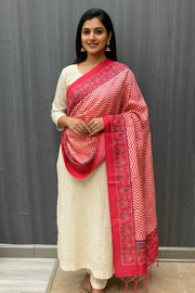 Woman wearing cream embroidered kurta with red and white zigzag patterned dupatta in indoor setting