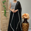 Woman in black and white embroidered Indian lehenga with sheer dupatta standing indoors near wooden screen and decorative vase
