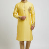 Man wearing a yellow embroidered Indian kurta with golden churidar pants and traditional sandals on white background
