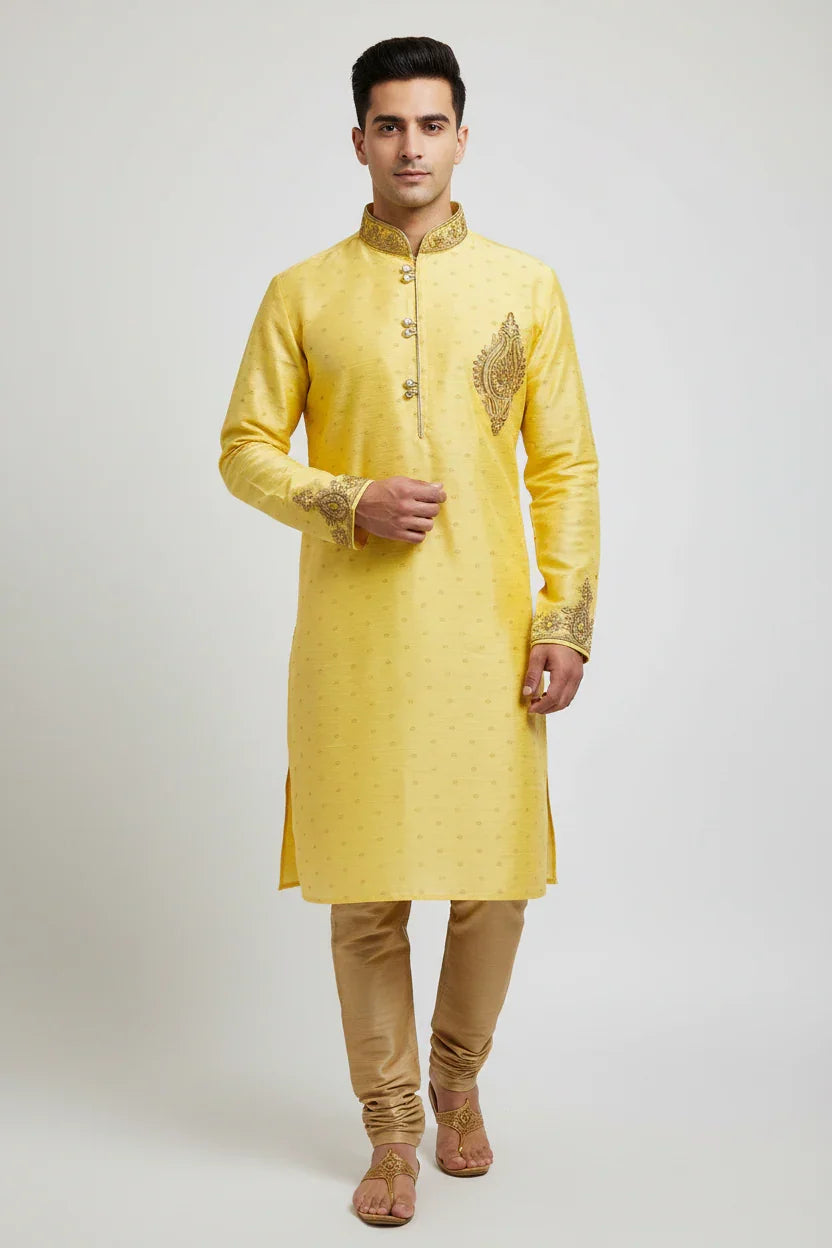 Man wearing a yellow embroidered Indian kurta with golden churidar pants and traditional sandals on white background