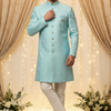 Man wearing a light blue sherwani with white pants in a decorated indoor setting.