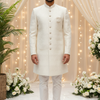 Man in a white traditional outfit standing in front of decorative lights and flowers.