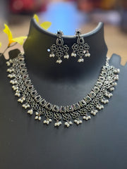 Intricate silver oxidized floral necklace and matching earrings with pearl drops displayed on black stand