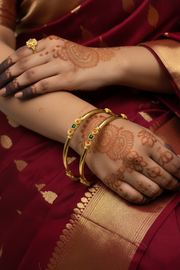 Close-up of hands wearing gold bangles and ring with floral henna, draped in maroon and gold saree fabric