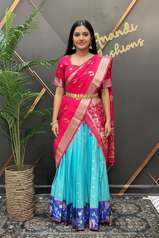 Woman in a red and blue saree standing in front of a decorative wall with 'Anandi Fashions' branding.