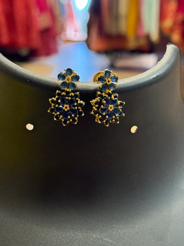 Gold earrings with blue floral gemstone design displayed on black stand at Anandi Fashions