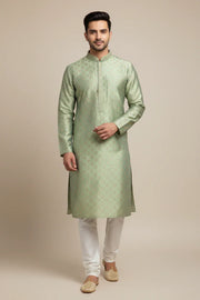 Man wearing light green embroidered Indian ethnic kurta with white churidar and traditional jutti shoes