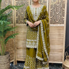 Woman in olive green embroidered Indian ethnic salwar kameez with dupatta, standing indoors by wooden screen