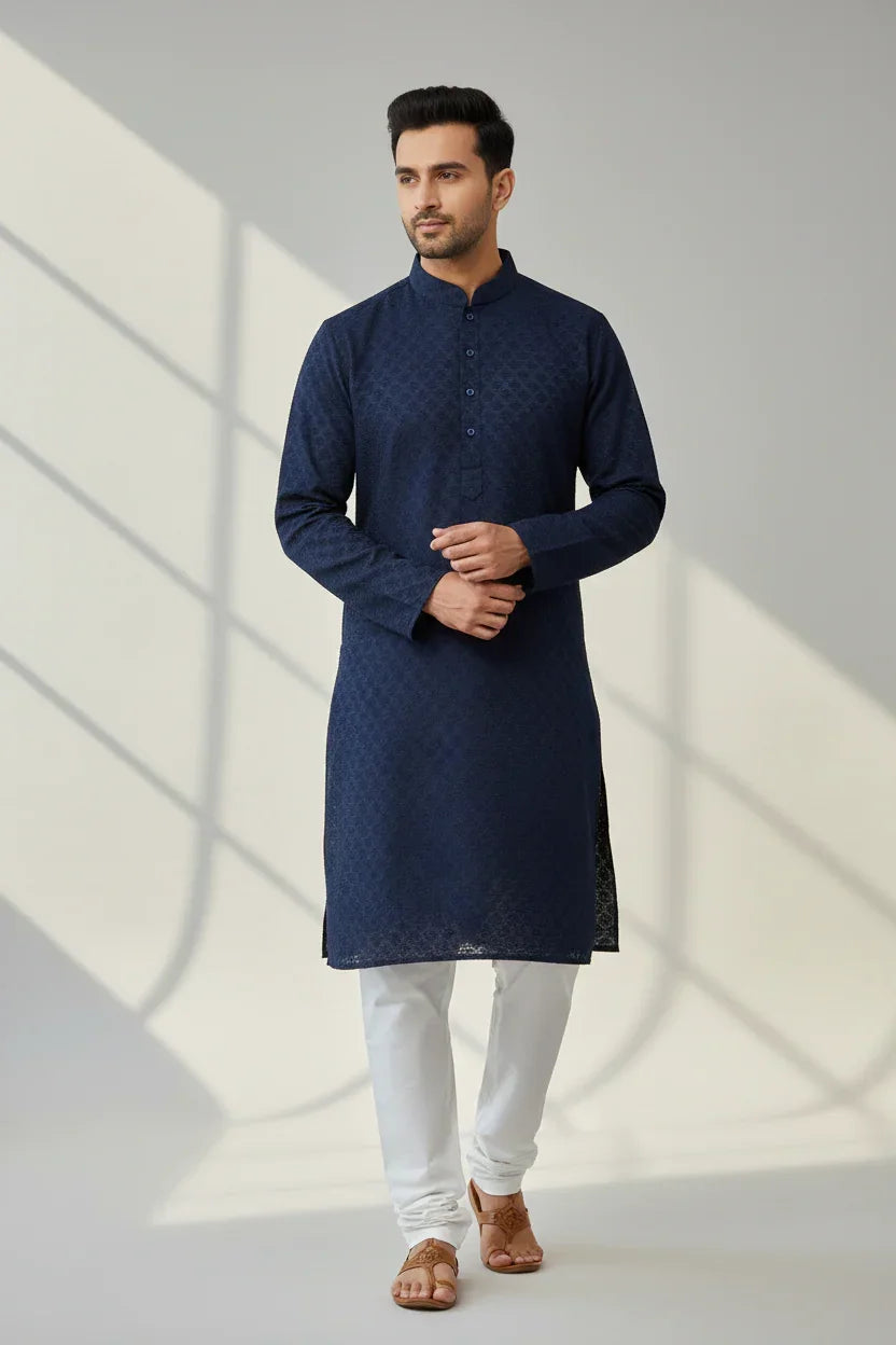 Man wearing navy blue Indian ethnic kurta with white churidar and brown sandals in minimal background