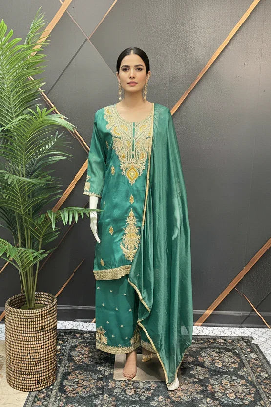 Mannequin wearing green Indian ethnic wear salwar kameez with gold embroidery and matching dupatta beside potted plant