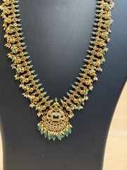 Traditional Indian gold necklace with green beads and intricate floral design displayed on black background