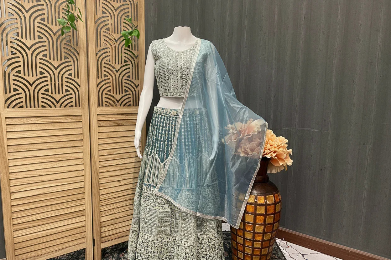 Mannequin displaying blue and cream embroidered Indian ethnic lehenga with sheer dupatta beside wooden screen and decorative vase