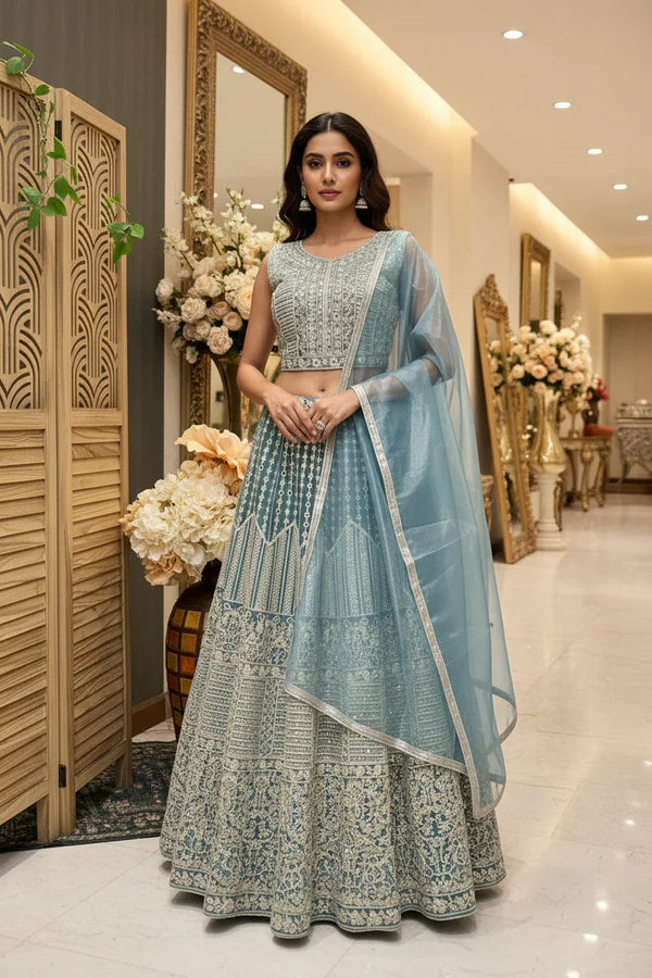 Woman modeling blue embroidered lehenga choli with sheer dupatta in elegant indoor setting at Anandi Fashions